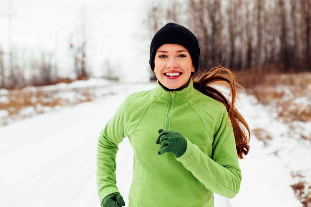 Smiling-young-woman-running-down-path-in-winter-running-gear.