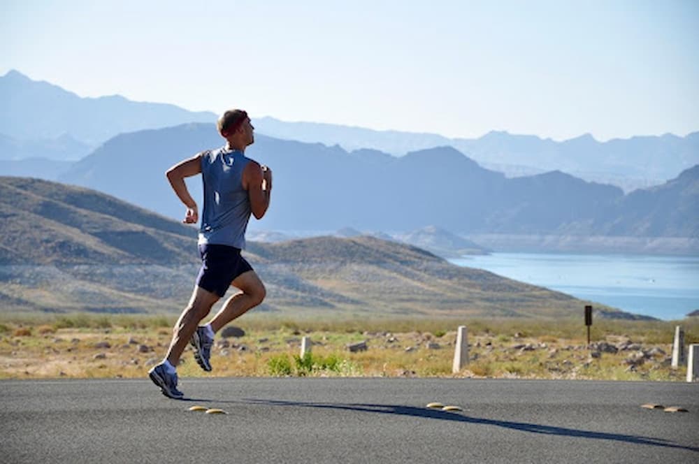 Athletic-man-running-down-road-beside-mountains-and-lake