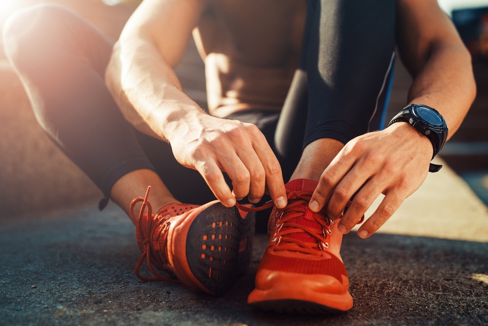 Athletic-runner-sitting-on-pavement-tying-laces-of-red-running-shoes