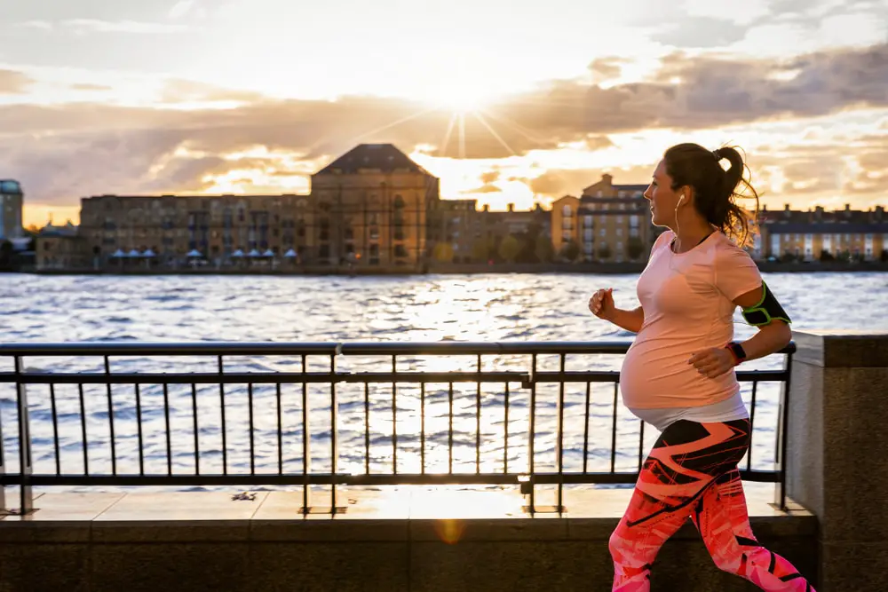 Active-pregnant-woman-running-along-river-outside-city