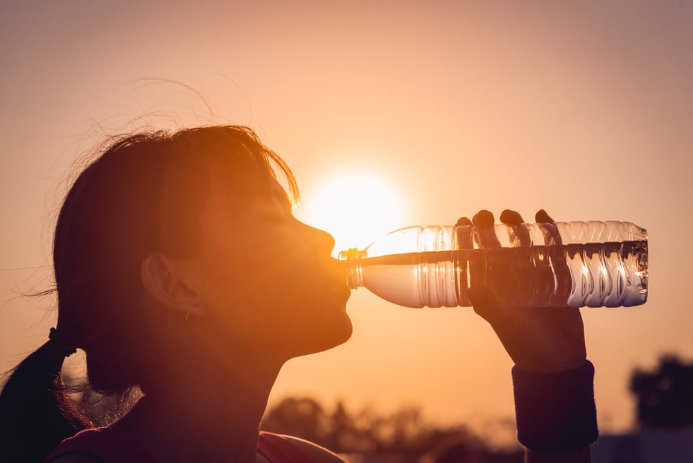 Woman-drinking-bottled-water-silhouetted-by-setting-sun