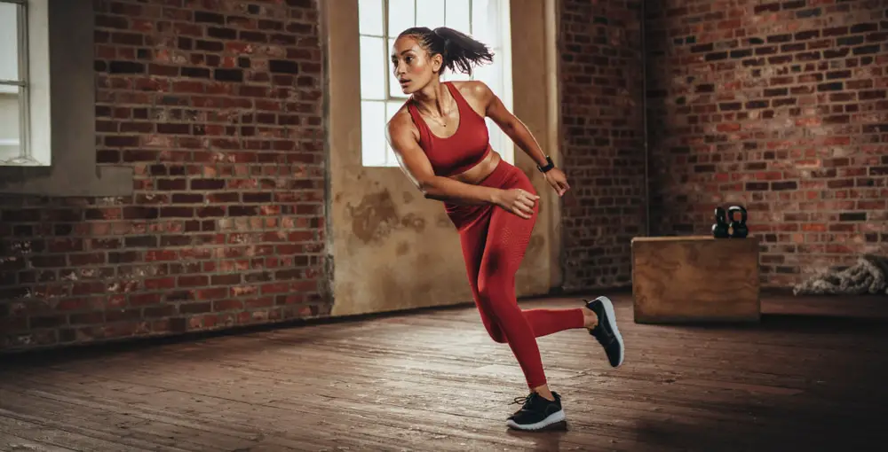 Woman-in-red-athletic-clothes-cross-training-in-room-with-brick-walls-and-wooden-floor