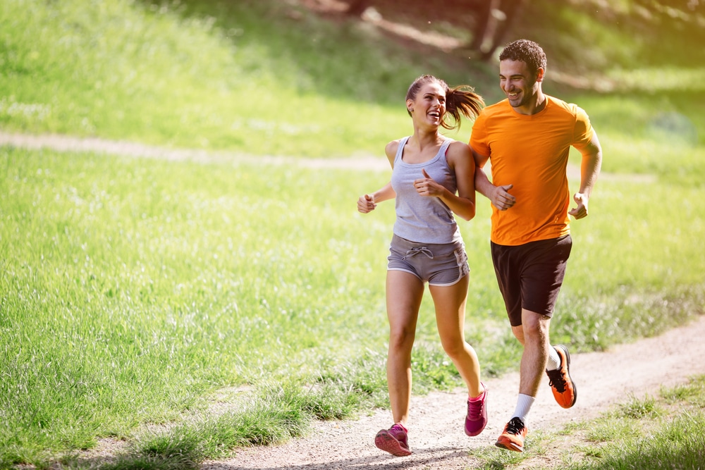 Young-couple-jogging-side-by-side-down-gravel-path-lined-by-grass