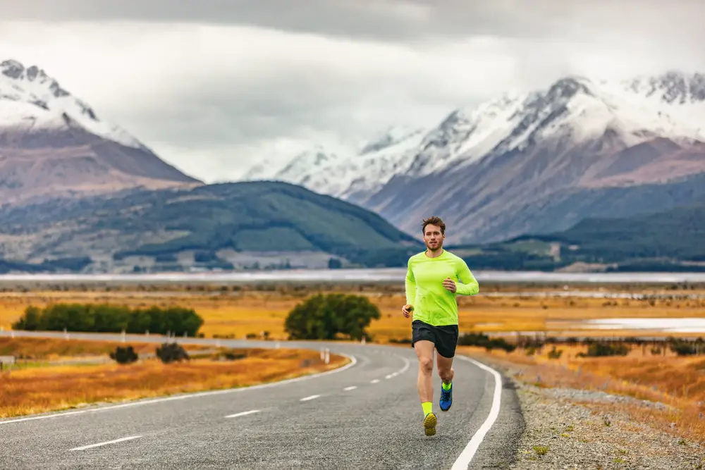 Man-in-reflective-green-athletic-shirt-running-down-curved-road-with-mountains-in-distance
