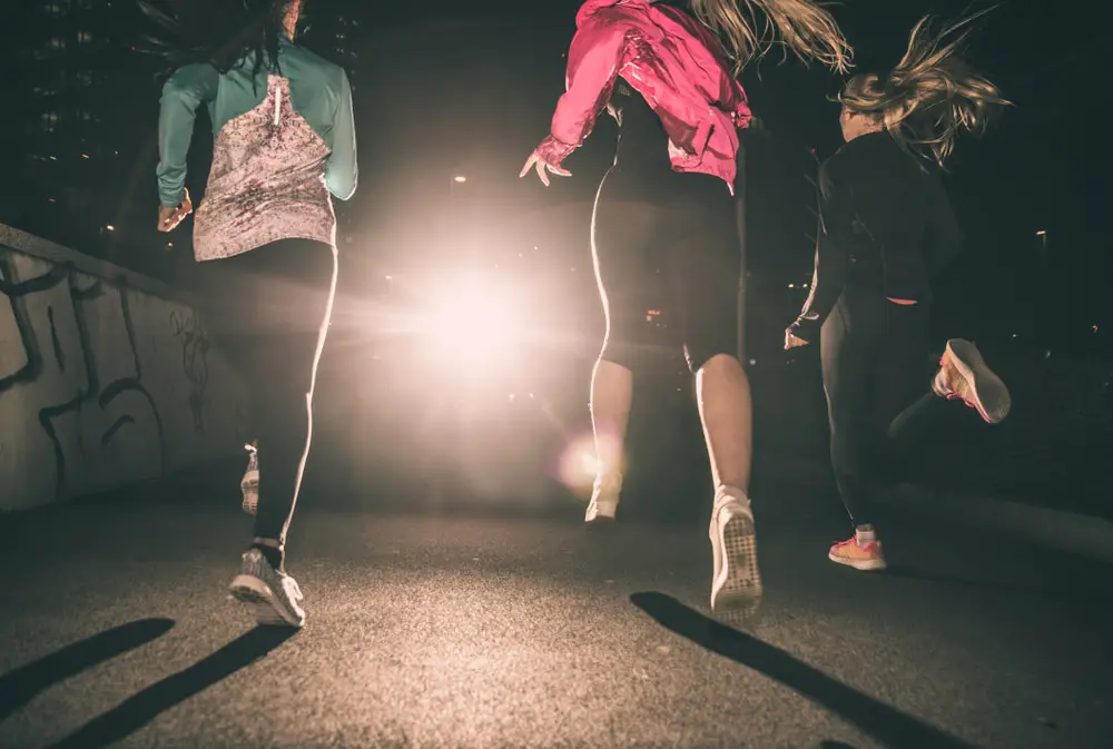 Three-women-running-at-night-on-paved-surface-with-light-shining-ahead-of-them