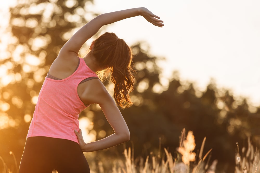 Young-fit-woman-in-athletic-clothing-stretching-in-grassy-area-at-sunrise