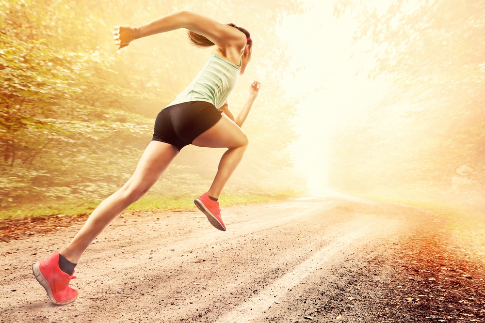 Female runner sprinting down dirt path into sunshine