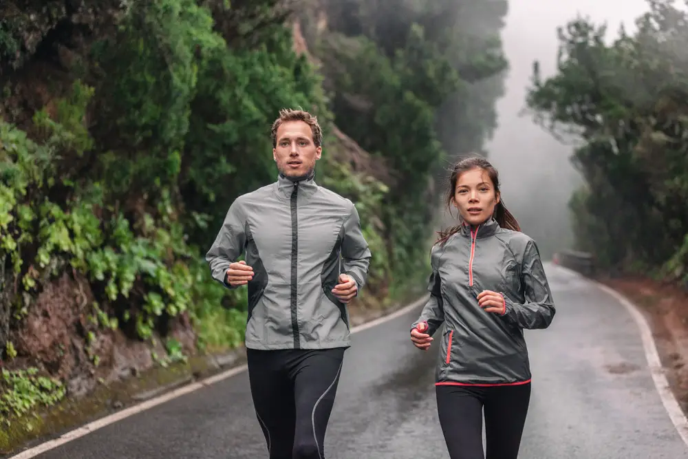 Man-and-woman-in-waterproof-running-jackets-and-leggings-running-down-road-through-fog