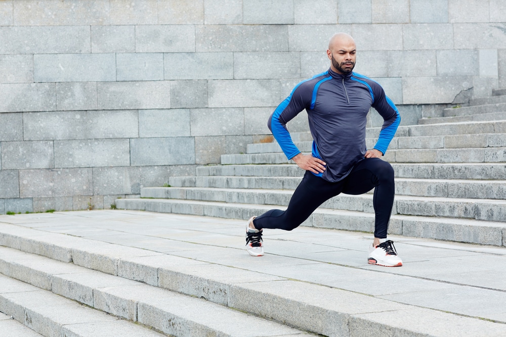 Man in athletic clothing doing lunges on outdoor staircase