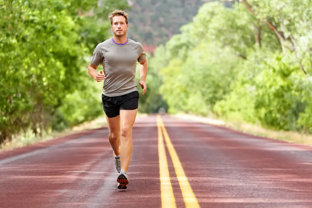 Man jogging down long red paved road in treed area