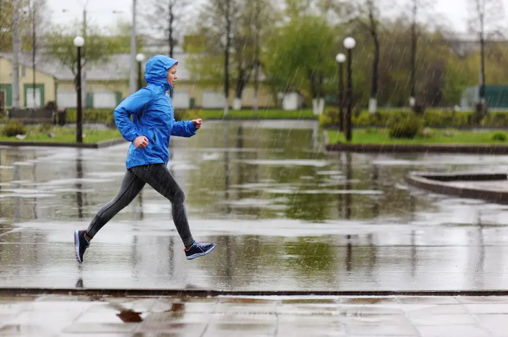 Woman in waterproof running jacket and hood running through park in the rain