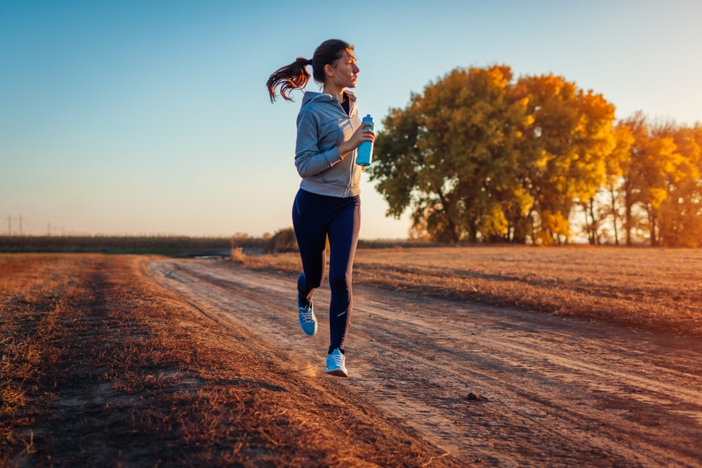 Woman running down dirt path at sunrise carrying running water bottle in her hand