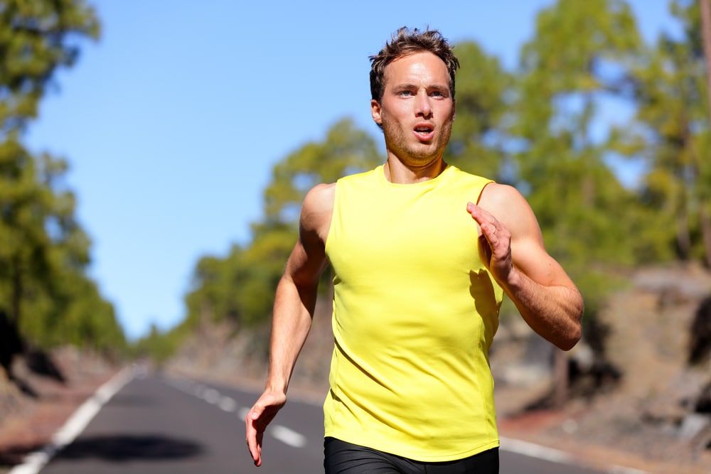 Man in yellow tank top sprinting down paved road on sunny day