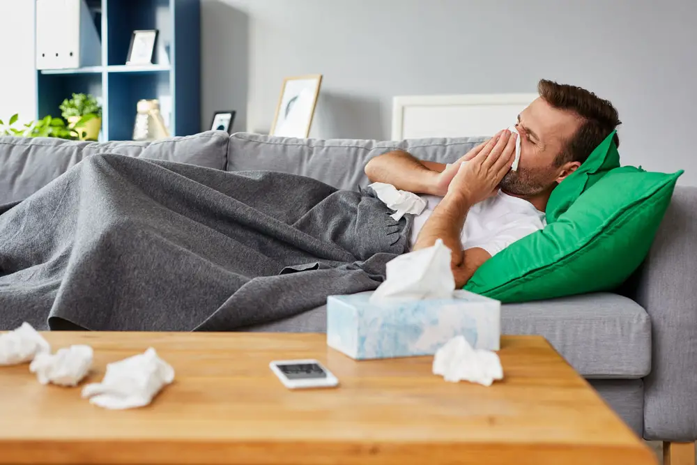 Man with a cold lying on sofa blowing nose
