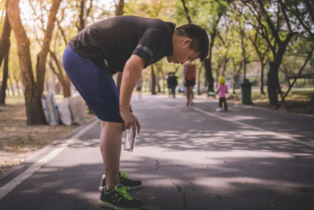 Young-Asian-man-resting-with-his-hands-on-his-knees-while-on-a-run
